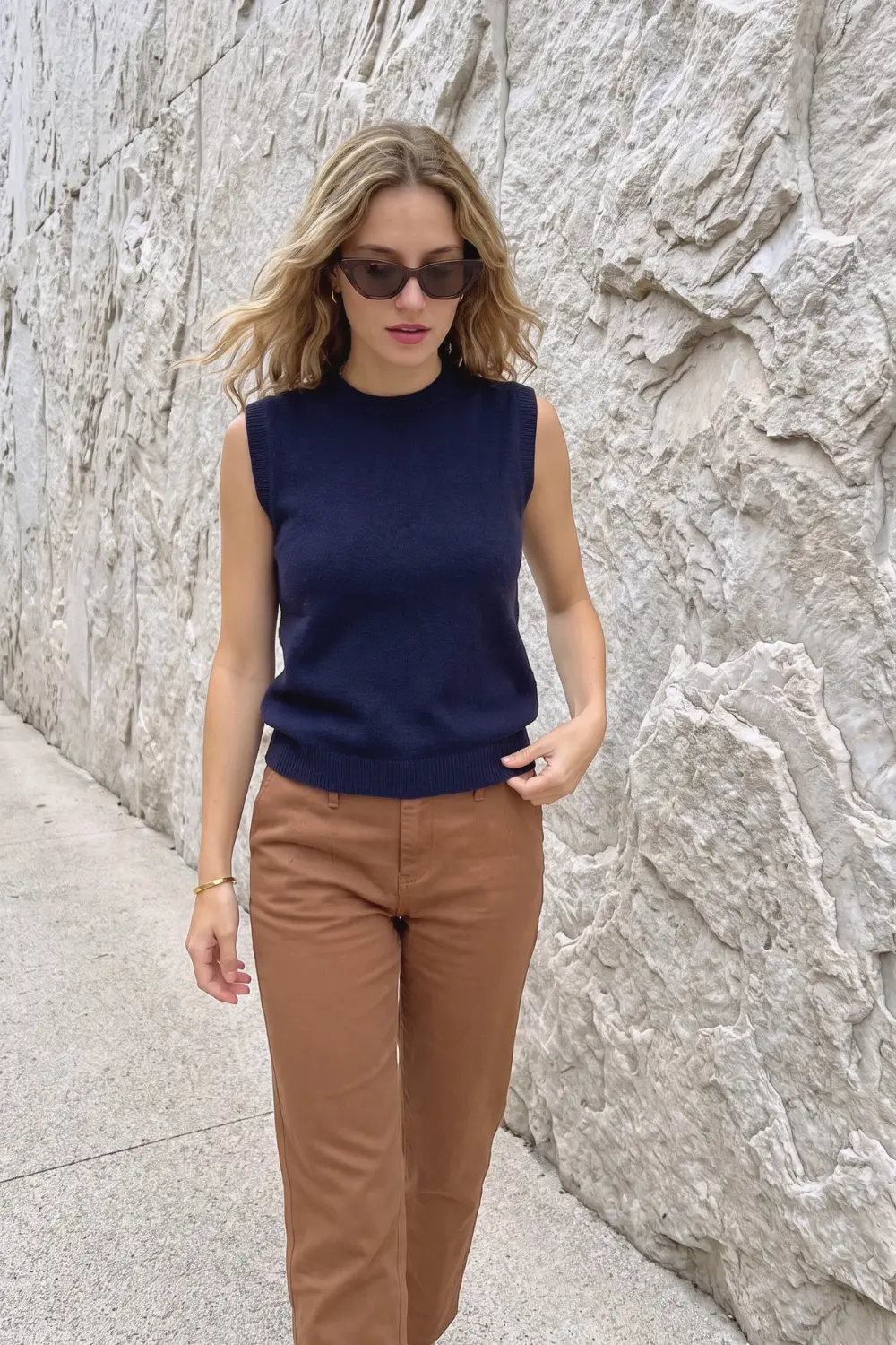 Woman in navy blue sleeveless crew neck knit vest top with tan camel straight leg chino trousers