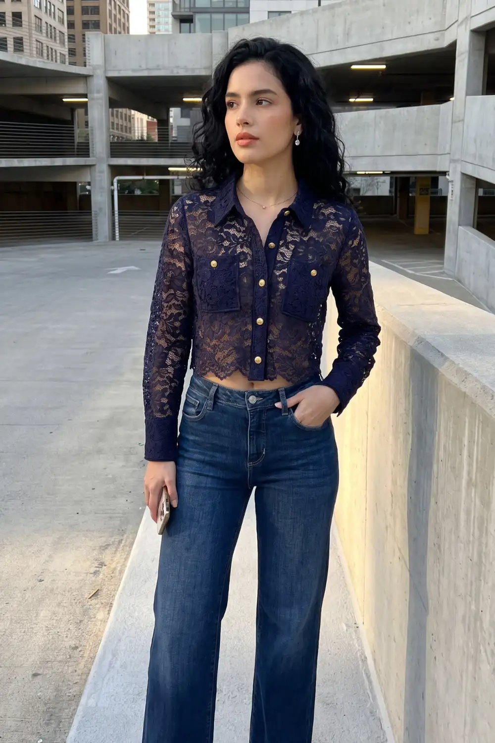 Woman in navy blue sheer lace crop shirt with gold buttons and medium wash wide leg jeans