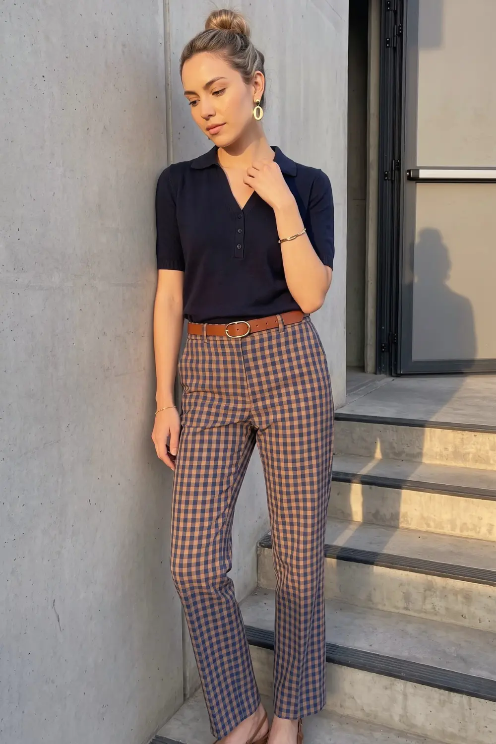 Woman in navy blue short sleeve polo knit top with navy brown gingham check straight leg trousers and tan belt