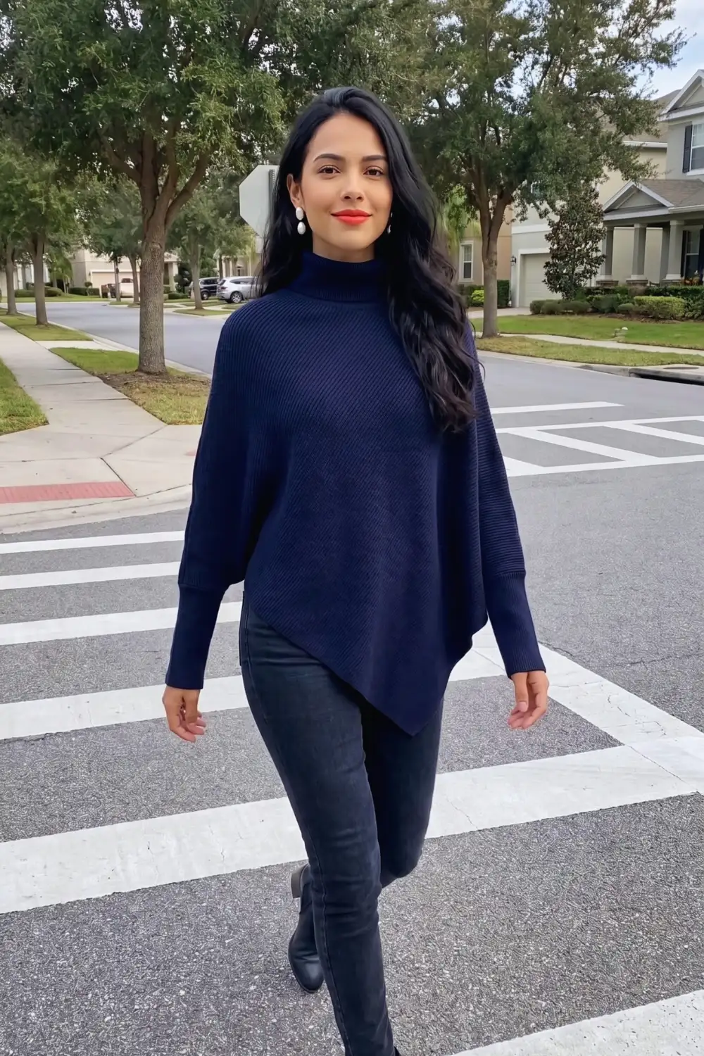 Woman in navy oversized poncho sweater with dark skinny jeans and black knee high boots