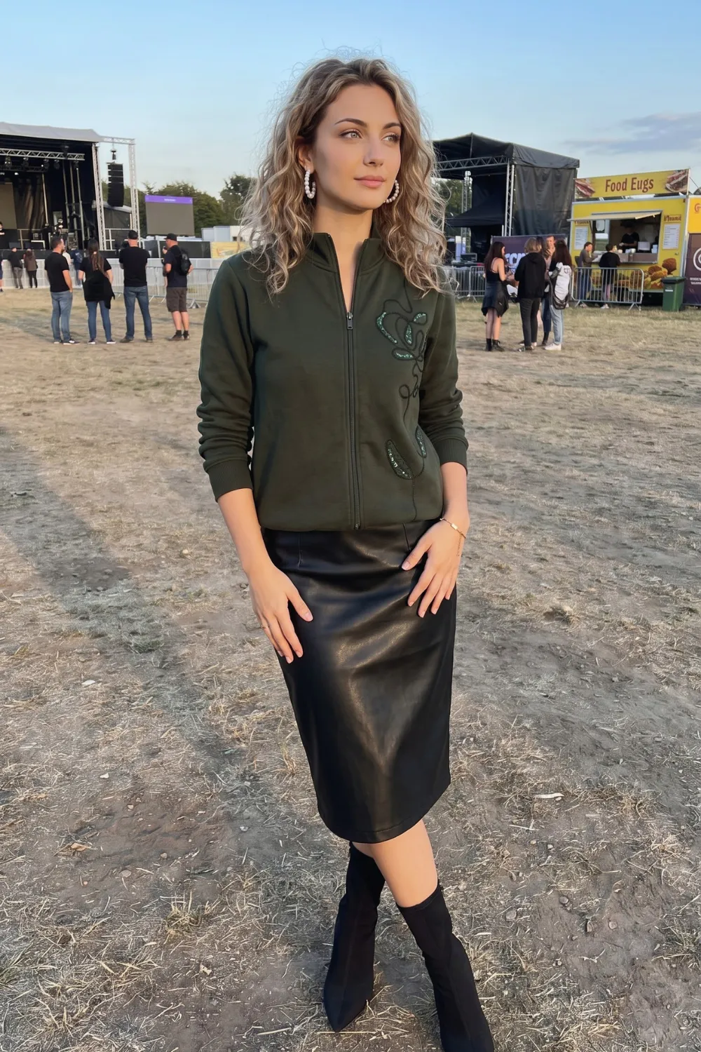 Woman in olive green zip jacket with black leather midi skirt and black ankle boots