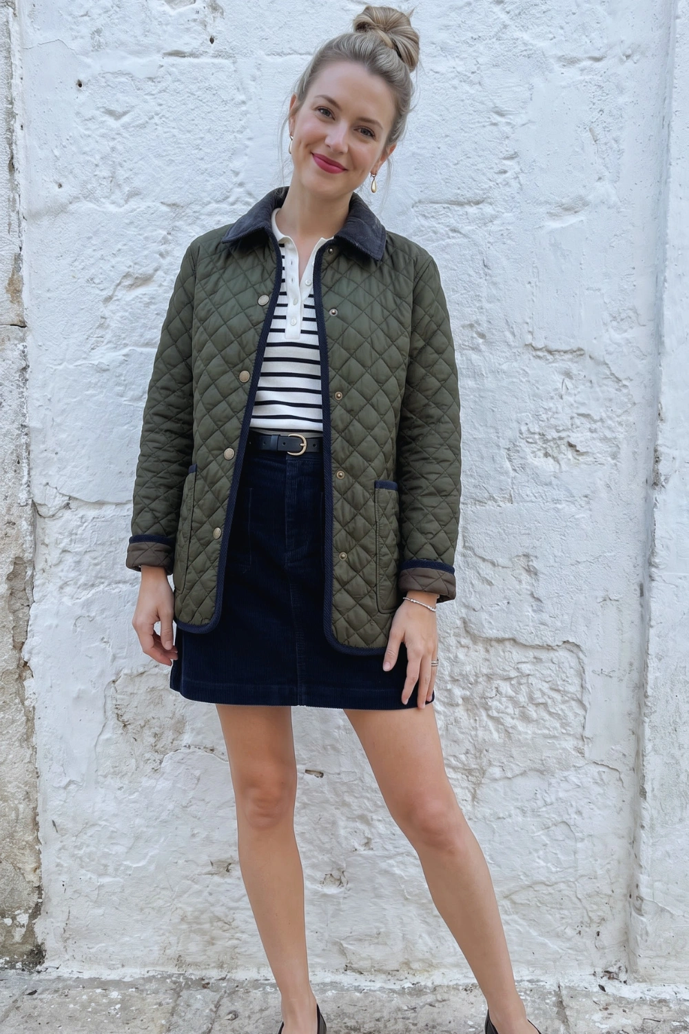 Woman in olive quilted jacket white stripe polo and navy corduroy mini skirt