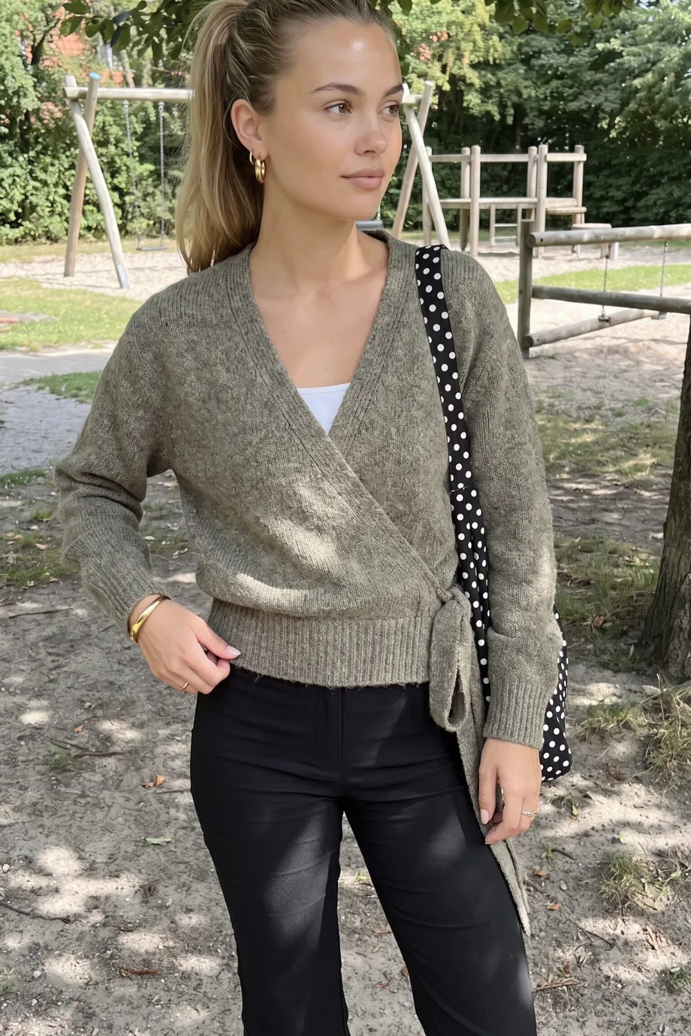 Woman in olive green wrap knit cardigan with black leather trousers