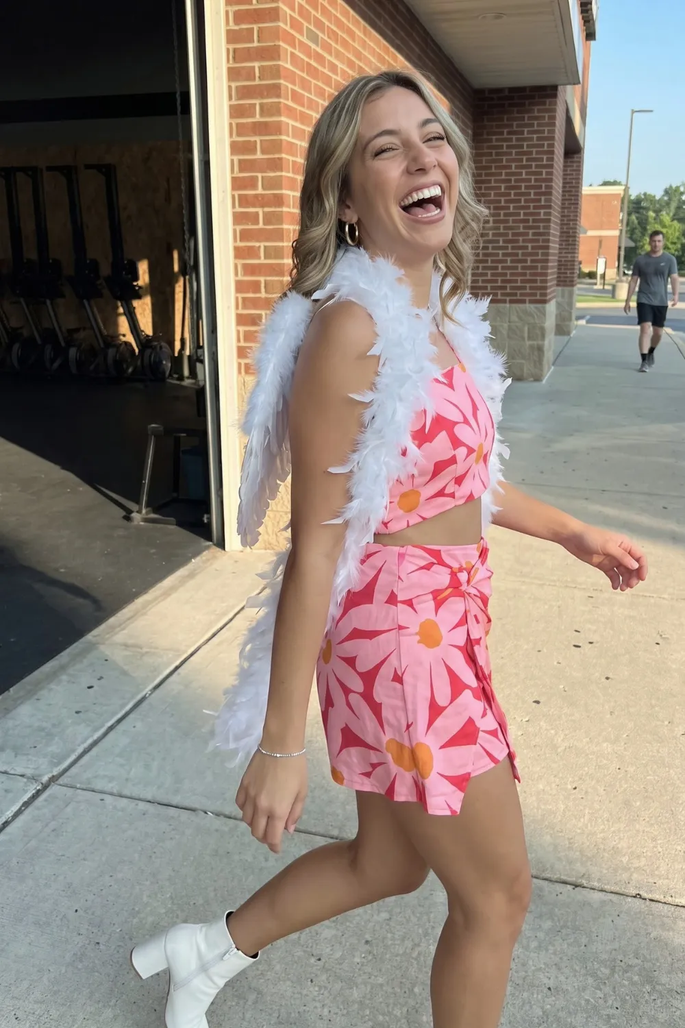 Woman in pink daisy print crop top and wrap mini skirt with white feather boa