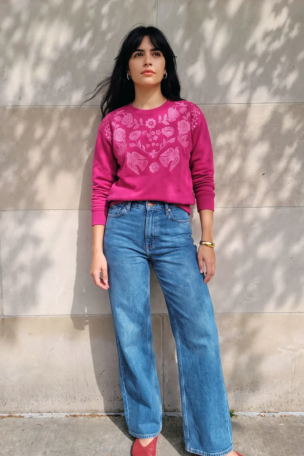 Woman in magenta pink floral bird embroidered sweatshirt and blue wide leg jeans