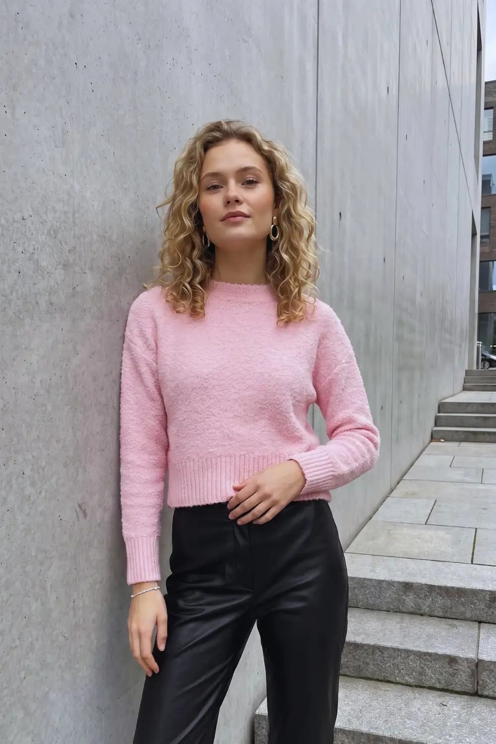 Woman in baby pink fluffy crop sweater with black faux leather wide leg trousers