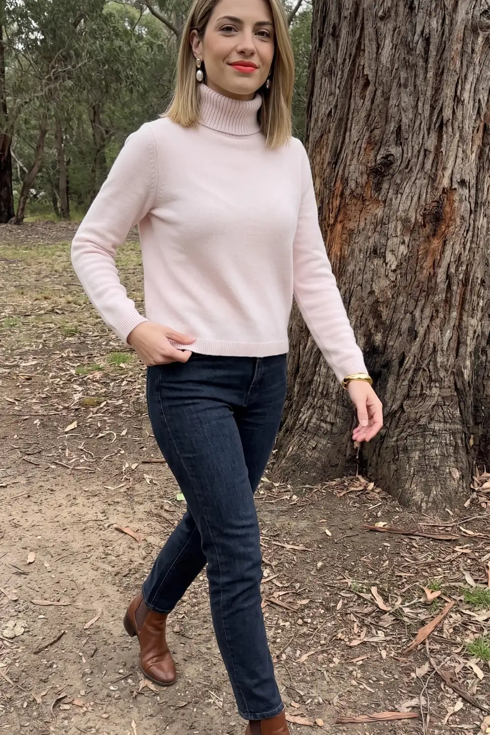 Woman in blush pink turtleneck sweater with dark wash skinny jeans and brown ankle boots