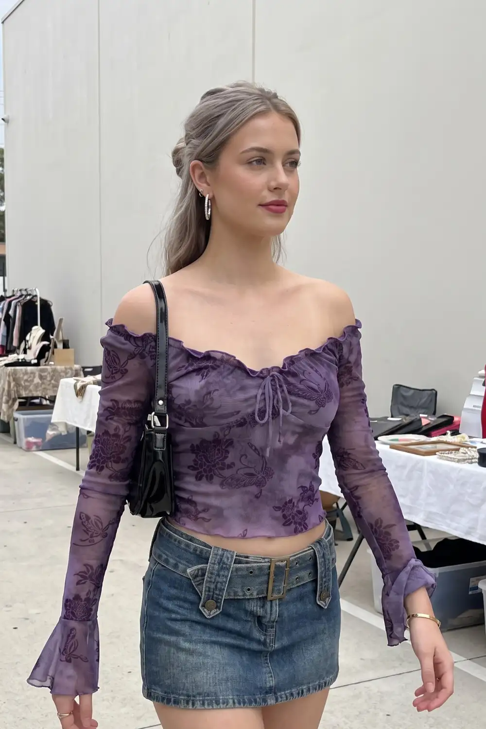 Woman in purple floral embroidered sheer mesh off shoulder top with denim mini skirt