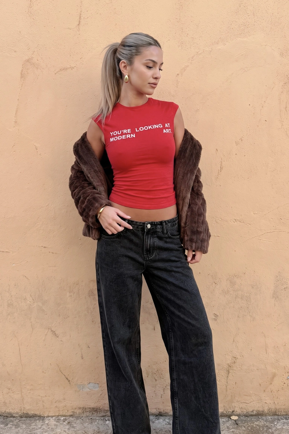 Woman in red graphic sleeveless crop top with dark brown faux fur cropped jacket and black washed wide leg jeans