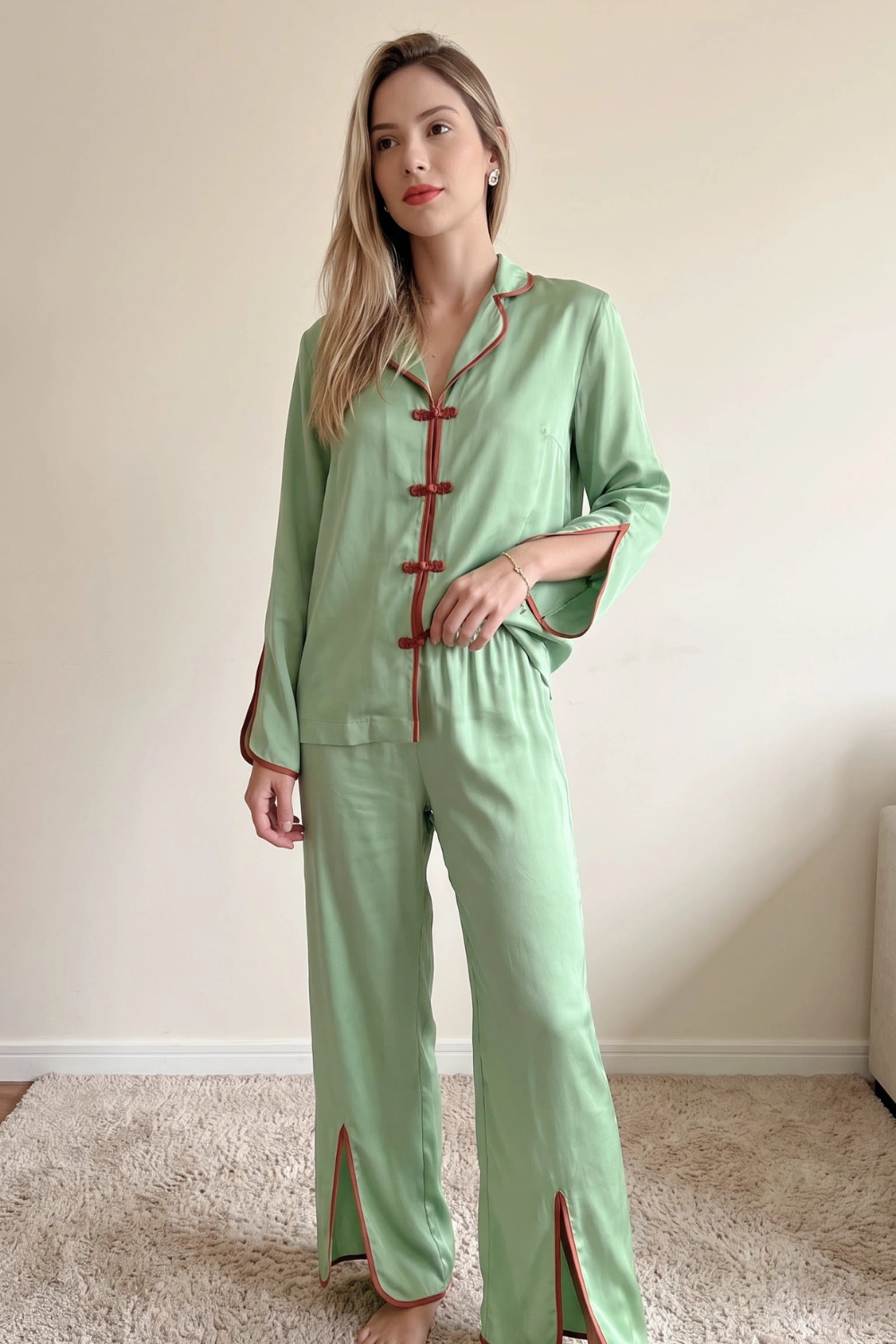 Woman in sage green satin long sleeve button down shirt with terracotta frog closure trim and wide leg split hem pants pajama set