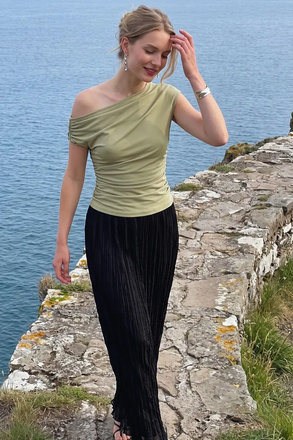 Woman in sage green one shoulder ruched top with black pleated velvet maxi skirt