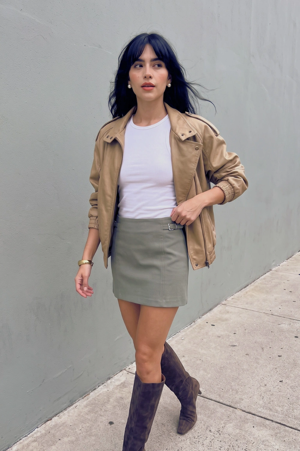 Woman in white top sage green belted mini skirt beige jacket and dark brown knee high boots