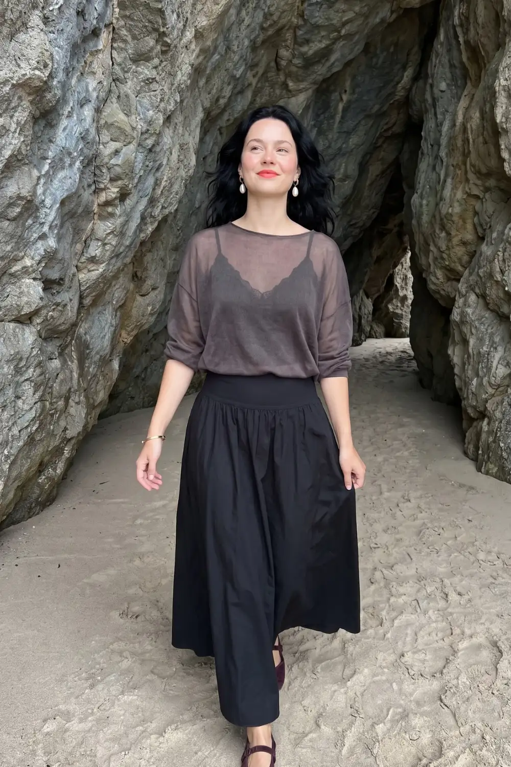 Woman in sheer dark brown bateau neck top over black lace bralette with black gathered maxi skirt