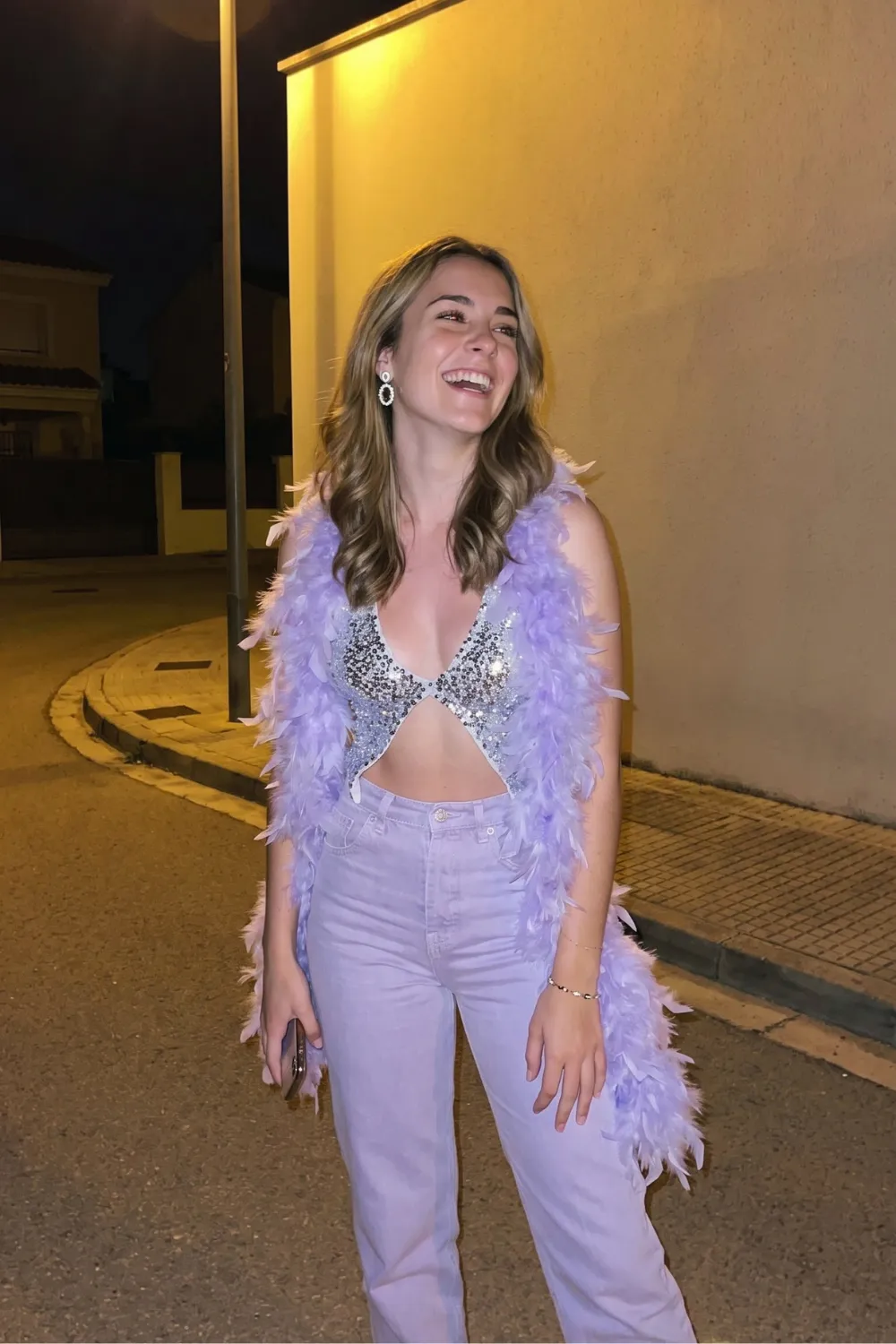 Woman in silver sequin bralette top with lavender wide leg jeans and lavender feather boa