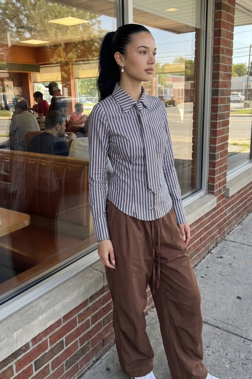 Woman in blue white striped bow collar fitted shirt with brown parachute pants