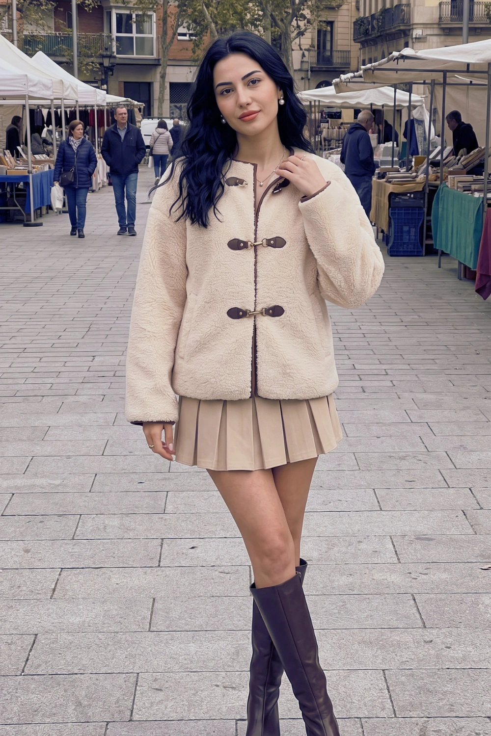 Woman in cream teddy shearling jacket with beige pleated mini skirt and dark brown knee high boots