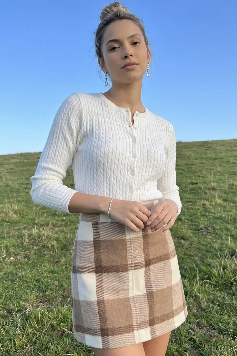 Woman in white cable knit cardigan with cream and camel plaid mini skirt