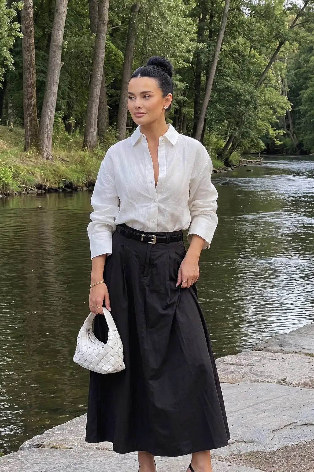 Woman in white linen oversized shirt with black pleated midi skirt and black belt