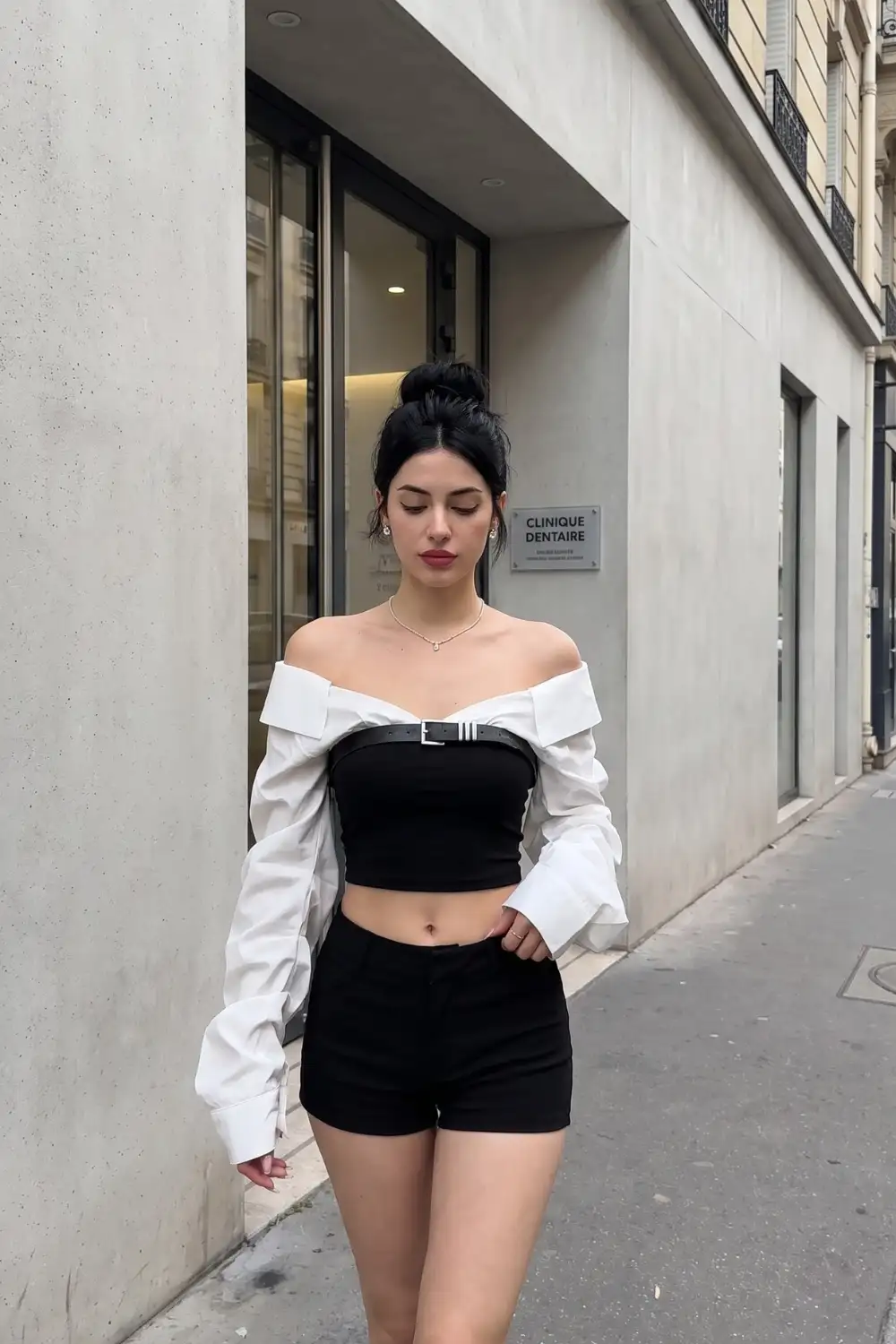 Woman in white off shoulder belted shirt over black bandeau crop top and black mini shorts